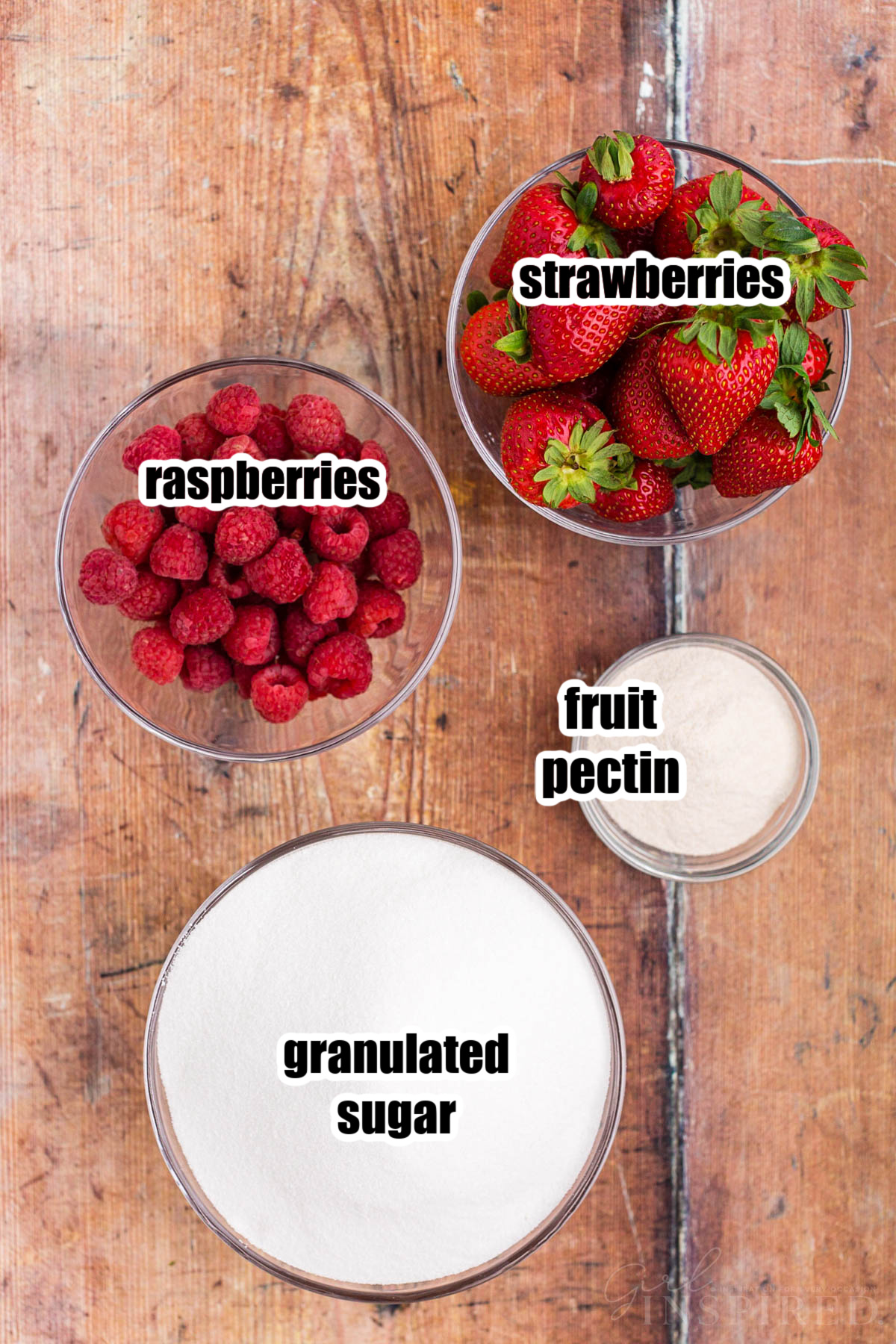 Bowl of fresh raspberries, bowl of fresh strawberries, bowl of white sugar, bowl of pectin, on top a wooden surface.
