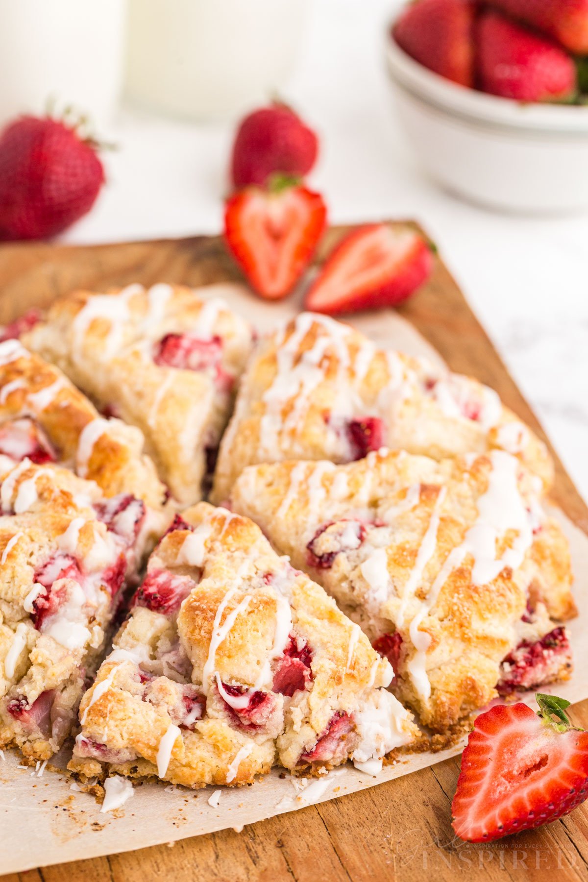Strawberry scones cut into wedges on cutting board with fresh strawberry halves.