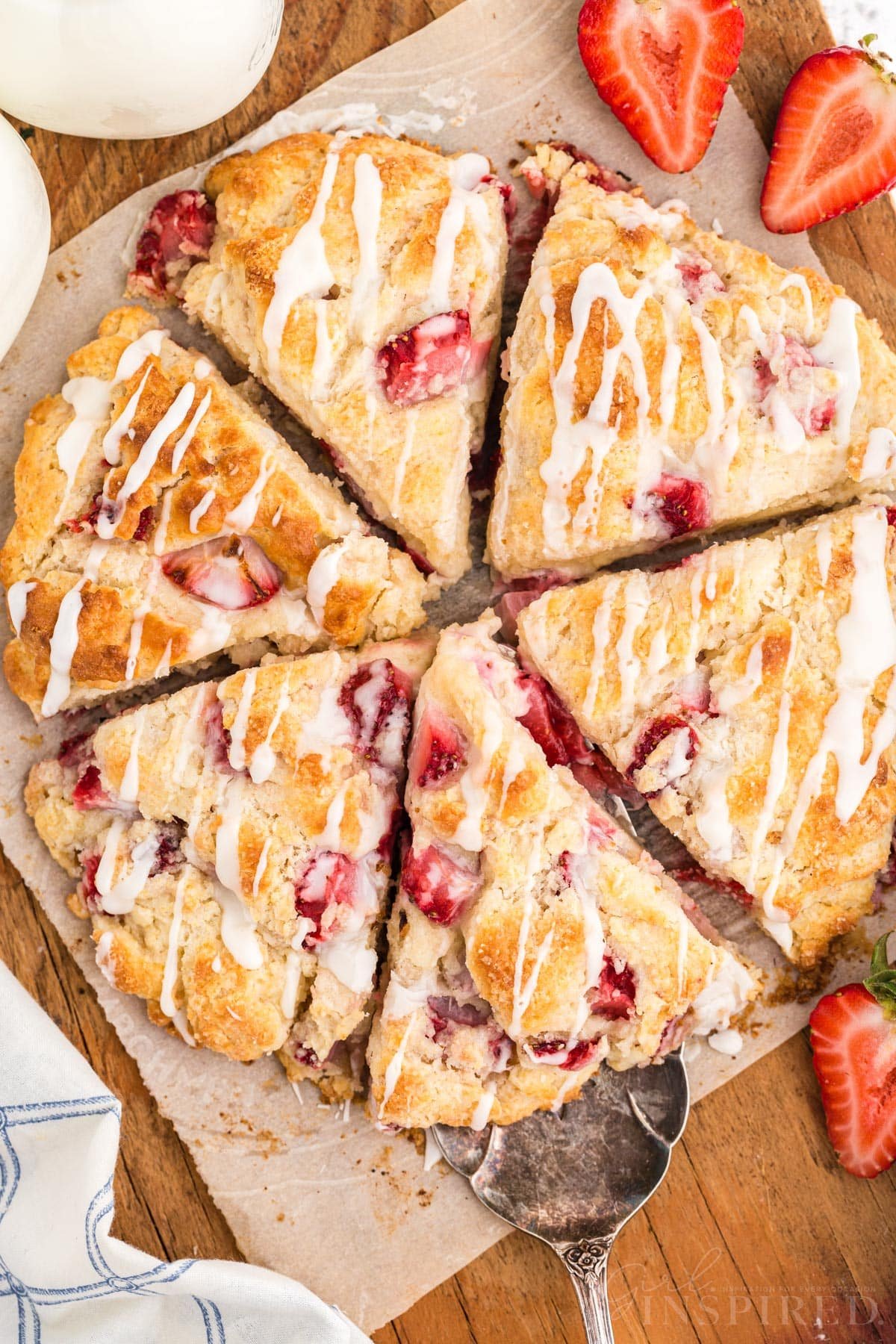 Baked strawberry scones on parchment paper atop a wooden kitchen board, freshly sliced strawberries.