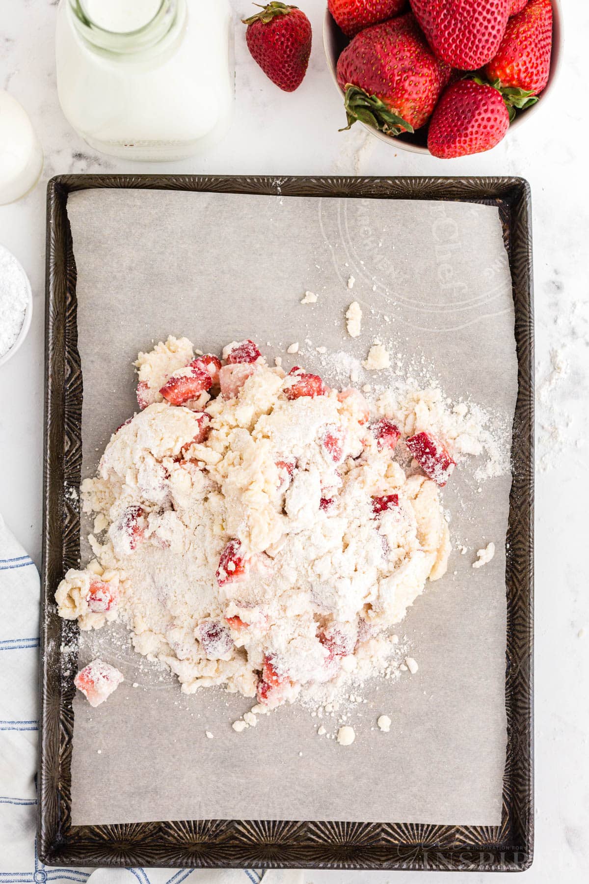 Mound of crumbly strawberry scone dough on baking sheet witih parchment paper.