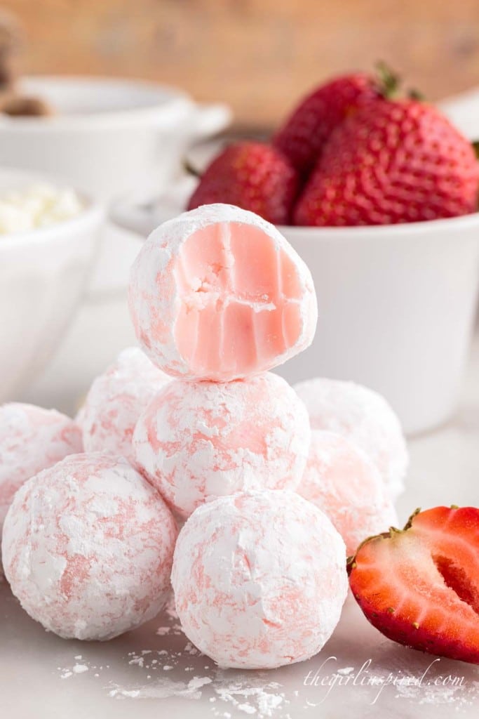 strawberry truffles in a stack with a bowl of whole strawberries in the background