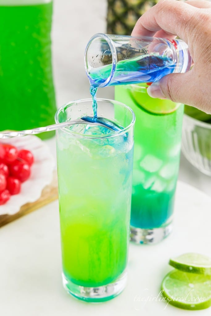 blue curacao poured from shot glass over an upside down spoon into glass filled with other drink ingredients
