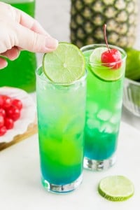 placing lime slice into glass filled with blue and green layered drink