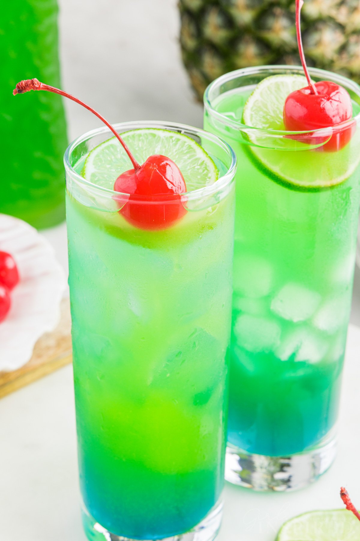 Finished tipsy mermaid drinks in glasses with lime round and maraschino cherry on top.