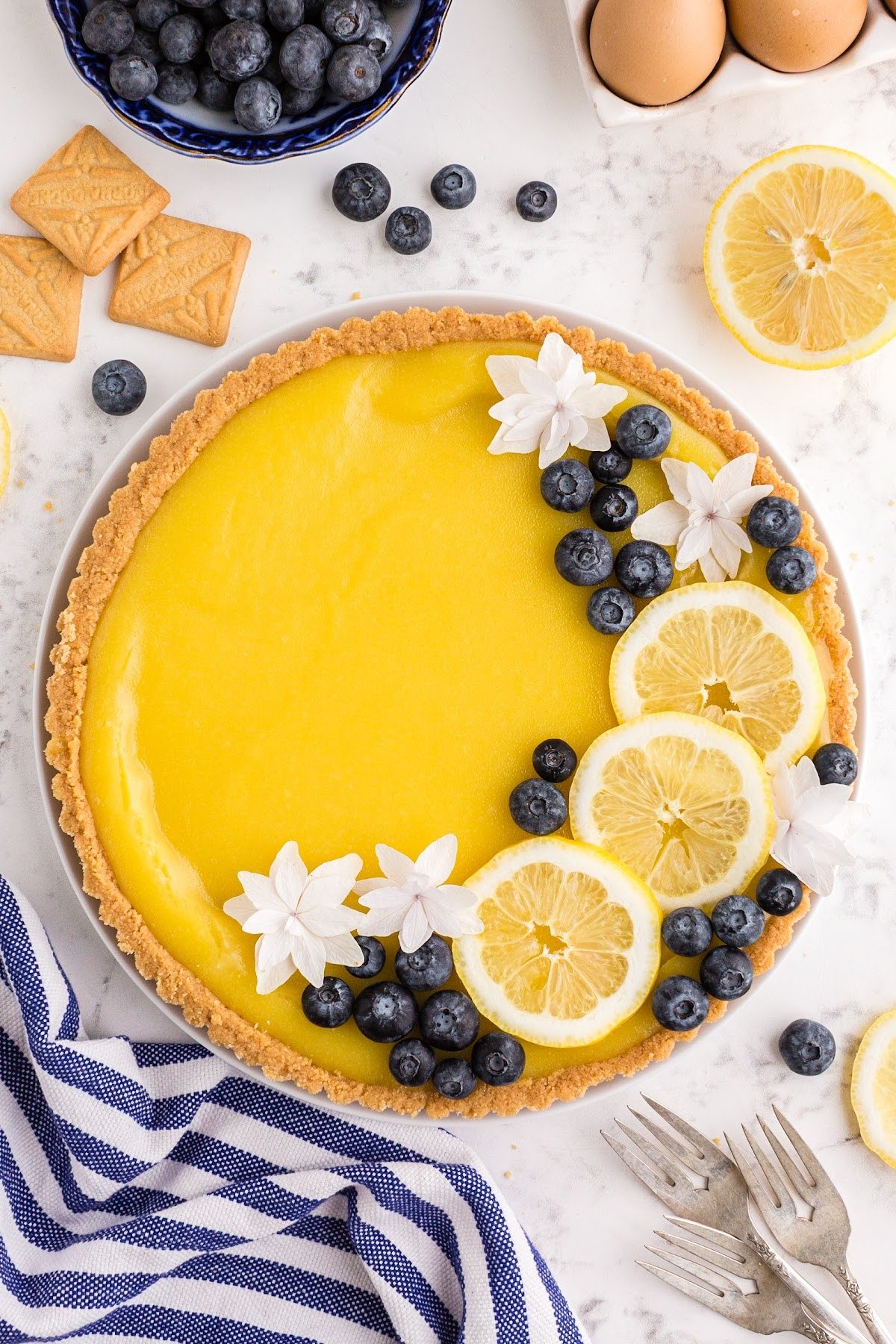 A garnished lemon curd tart with berries, editable flowers, and lemon slices.
