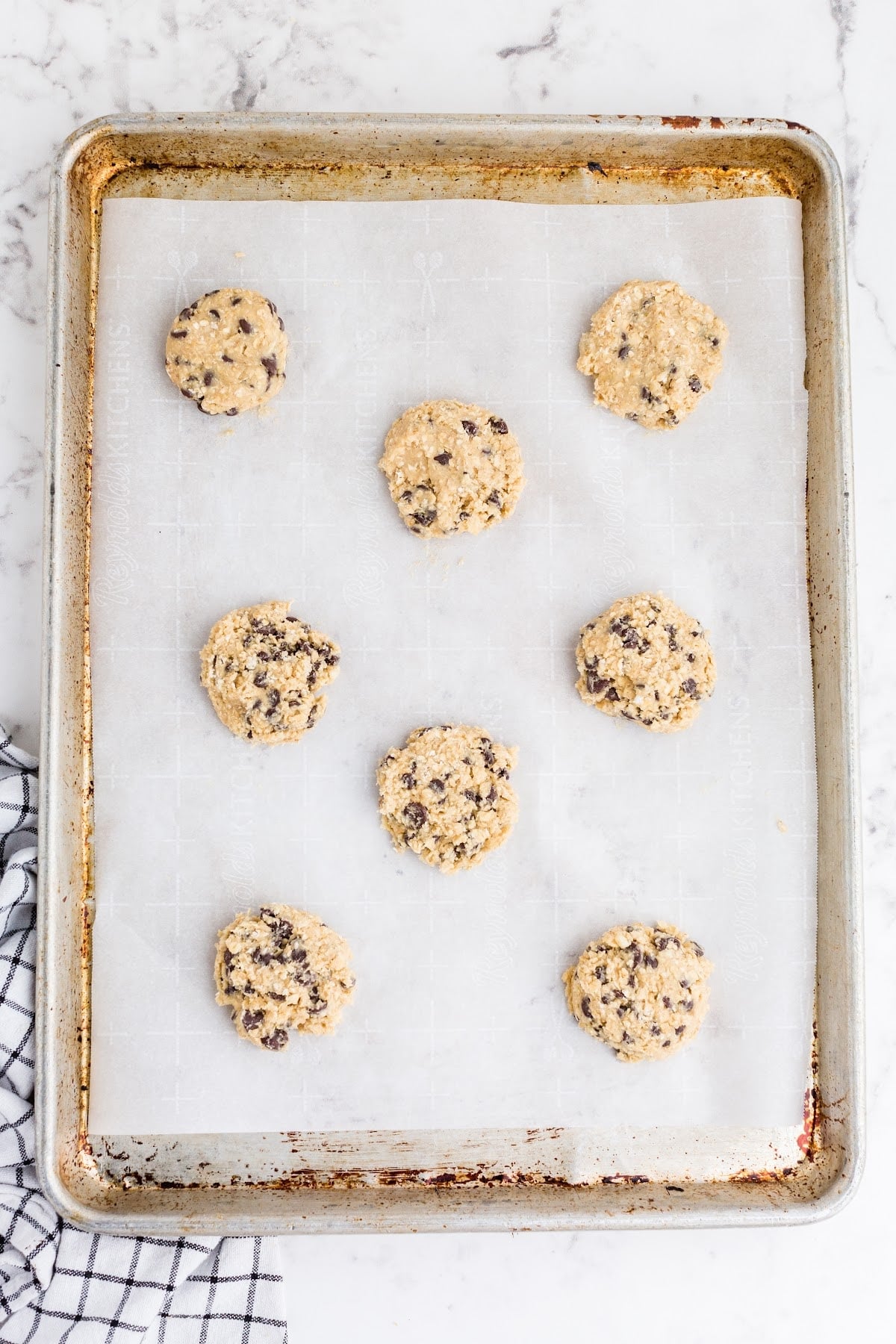 Oatmeal chocolate chip cookie dough balls arranged on baking sheet and pressed down/slightly flattened.