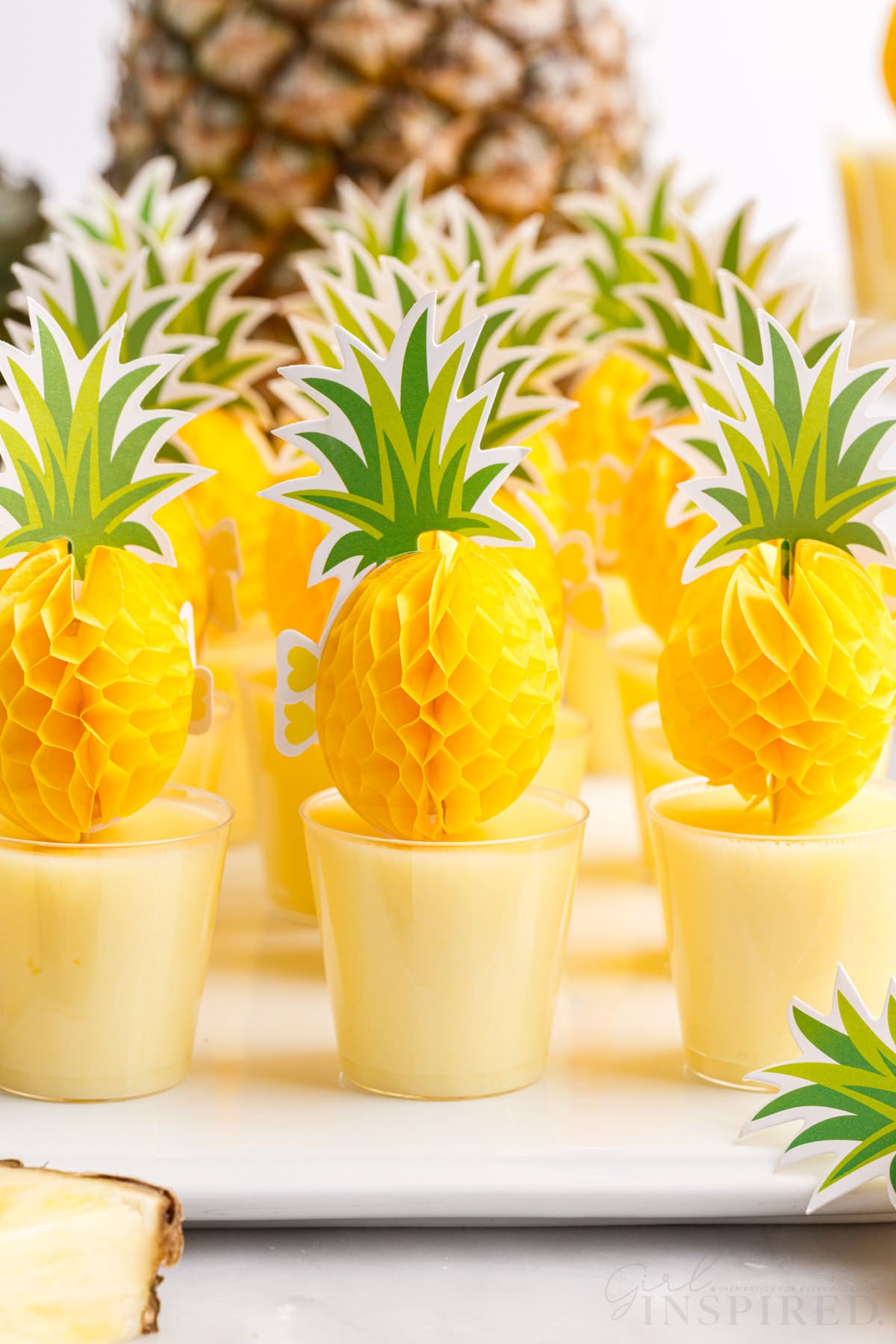 dole whip pineapple jello shots lined up on a tray next to a fresh pineapple