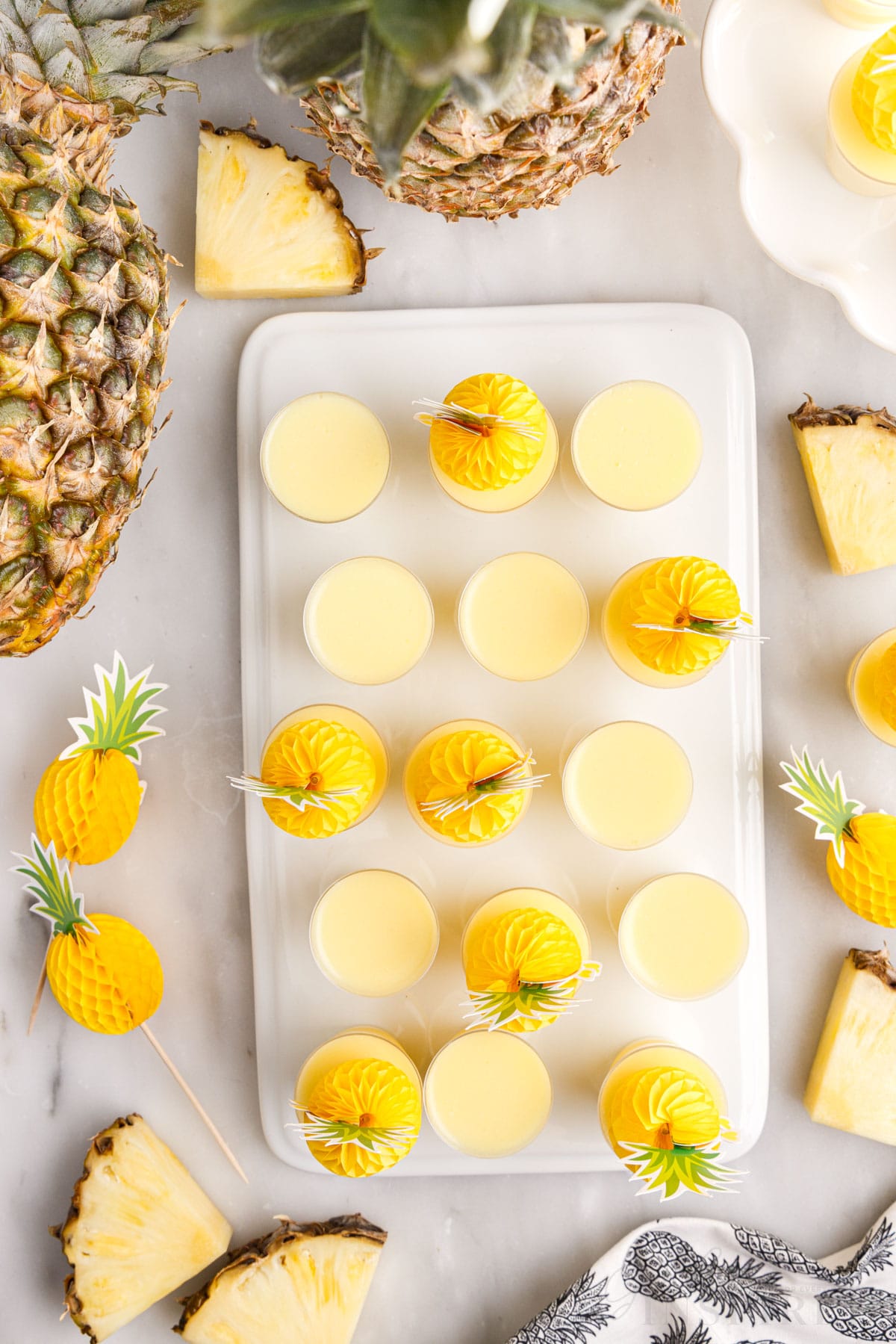 top view of dole whip jello shots on a tray next to pineapple slices