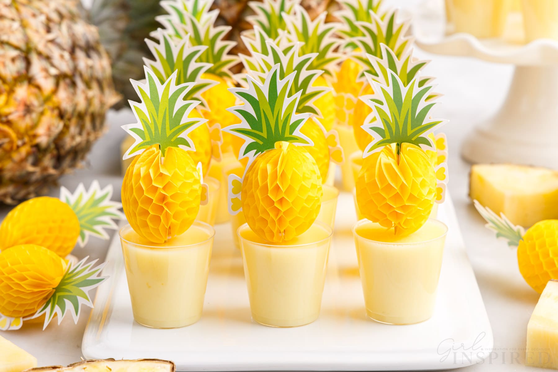 dole whip jello shots on a serving tray next to a whole pineapple
