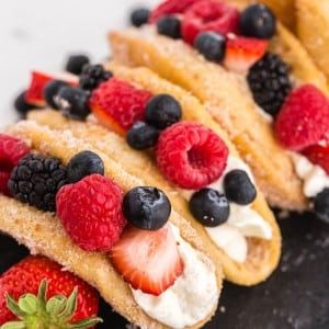 Close up of mixed berry cheesecake tacos on a black slate stone tile decorated with fresh berries