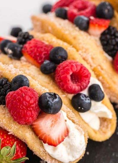 Close up of mixed berry cheesecake tacos on a black slate stone tile decorated with fresh berries