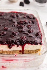 No bake blackberry cheesecake in a baking dish with slices removed, bowl of fresh blackberries, on a white marble countertop.