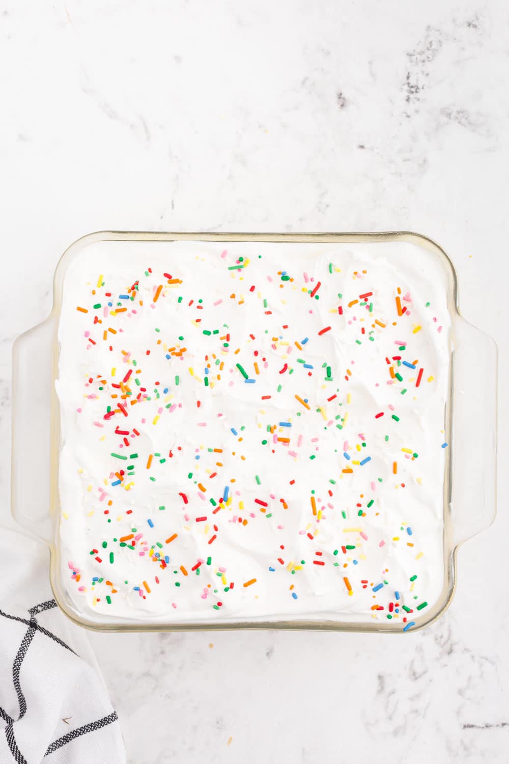 Square baking dish with dessert topped with whipped cream and rainbow sprinkles.