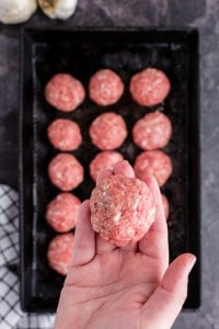 holding a raw meatball over the rest that are on the pan