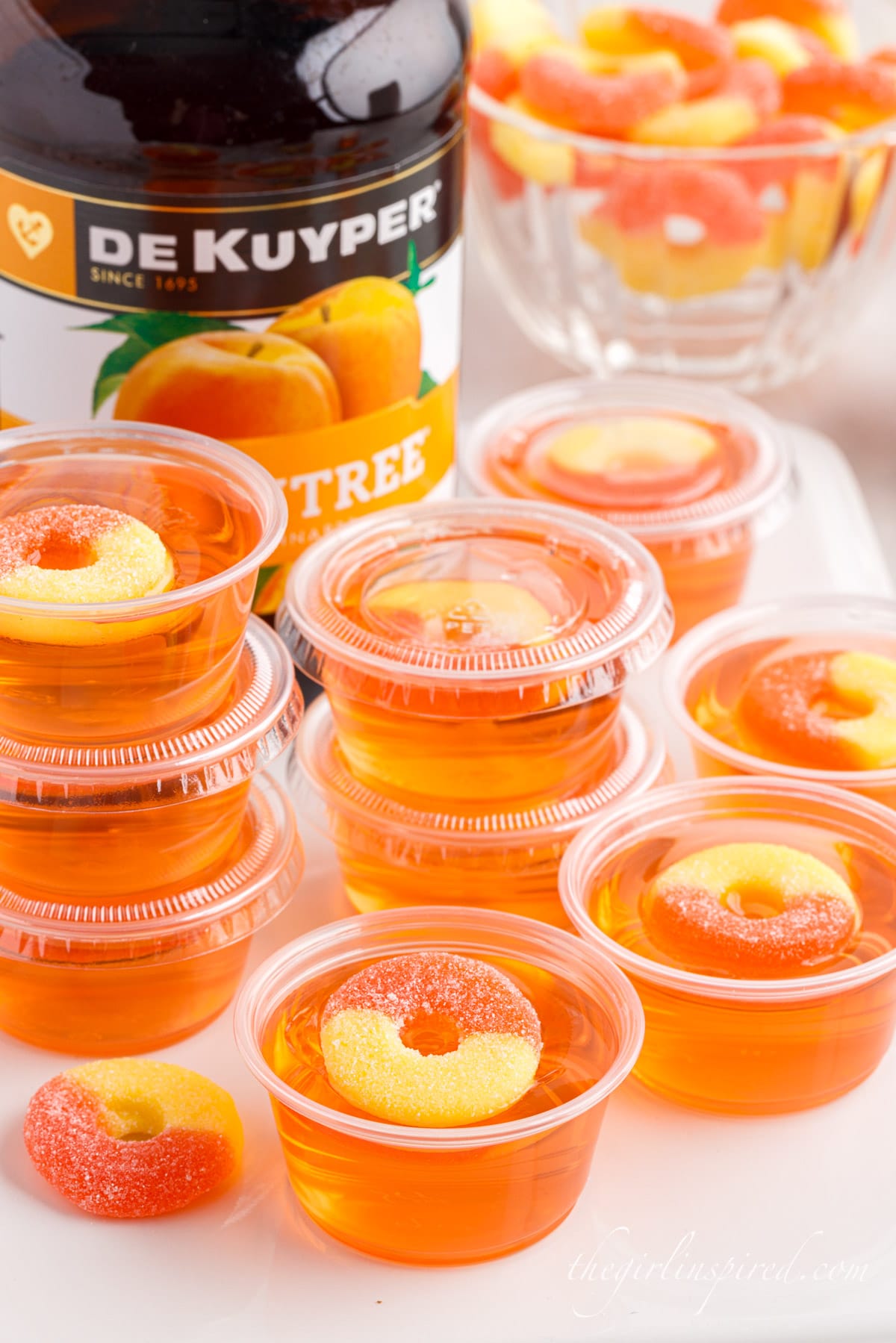 peach jello shots next to a liquor bottle topped with peach ring candies
