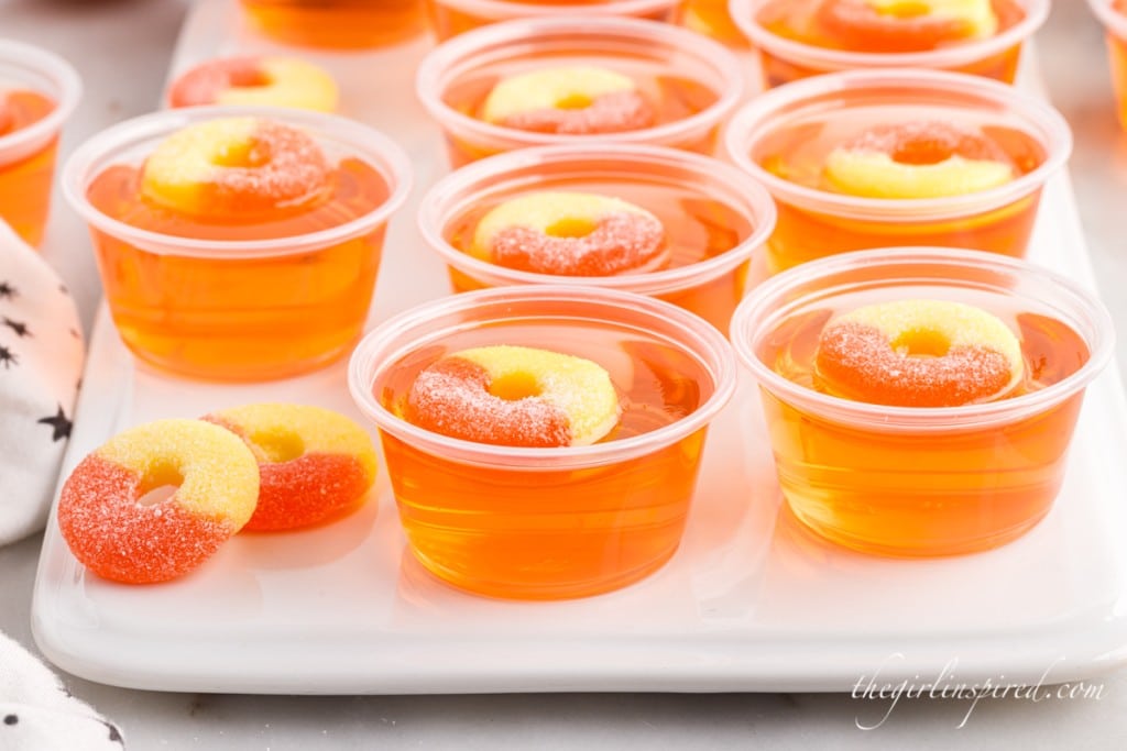 close up of peach jello shots in plastic cups topped with circle candies