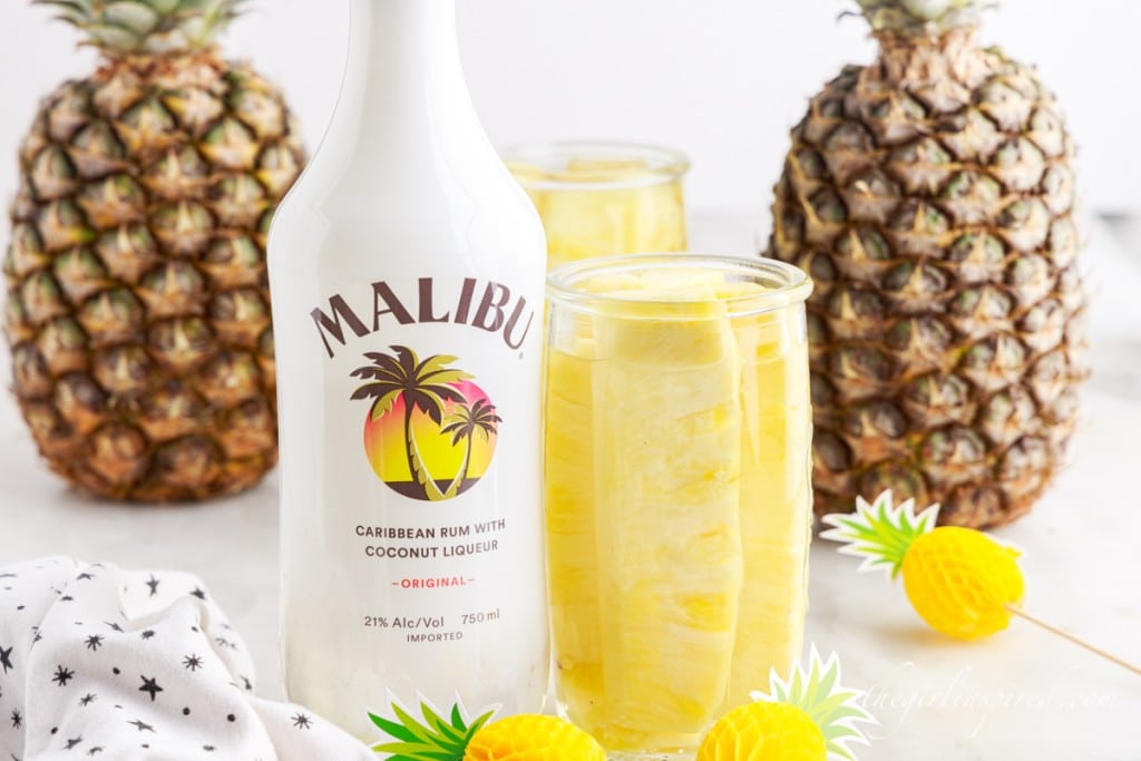 Pineapple Spears in Malibu Rum next to the liquor bottle and whole pineapple