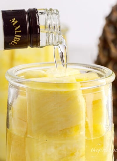 pineapple spears in a jar of malibu rum next to a whole pineapple