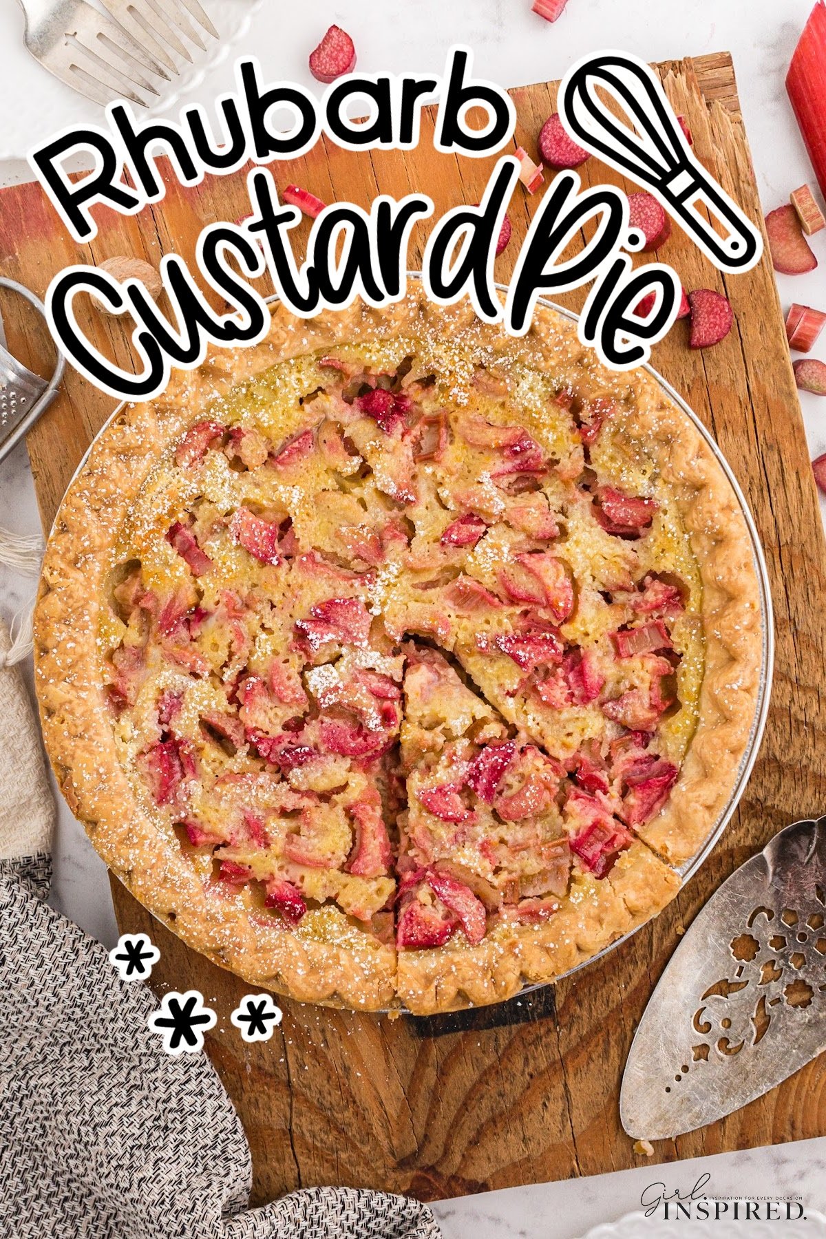 Whole baked rhubarb custard pie on a wooden board atop a white marble surface with a kitchen cloth in the left bottom corner and chopped rhubarb scattered around the pie.