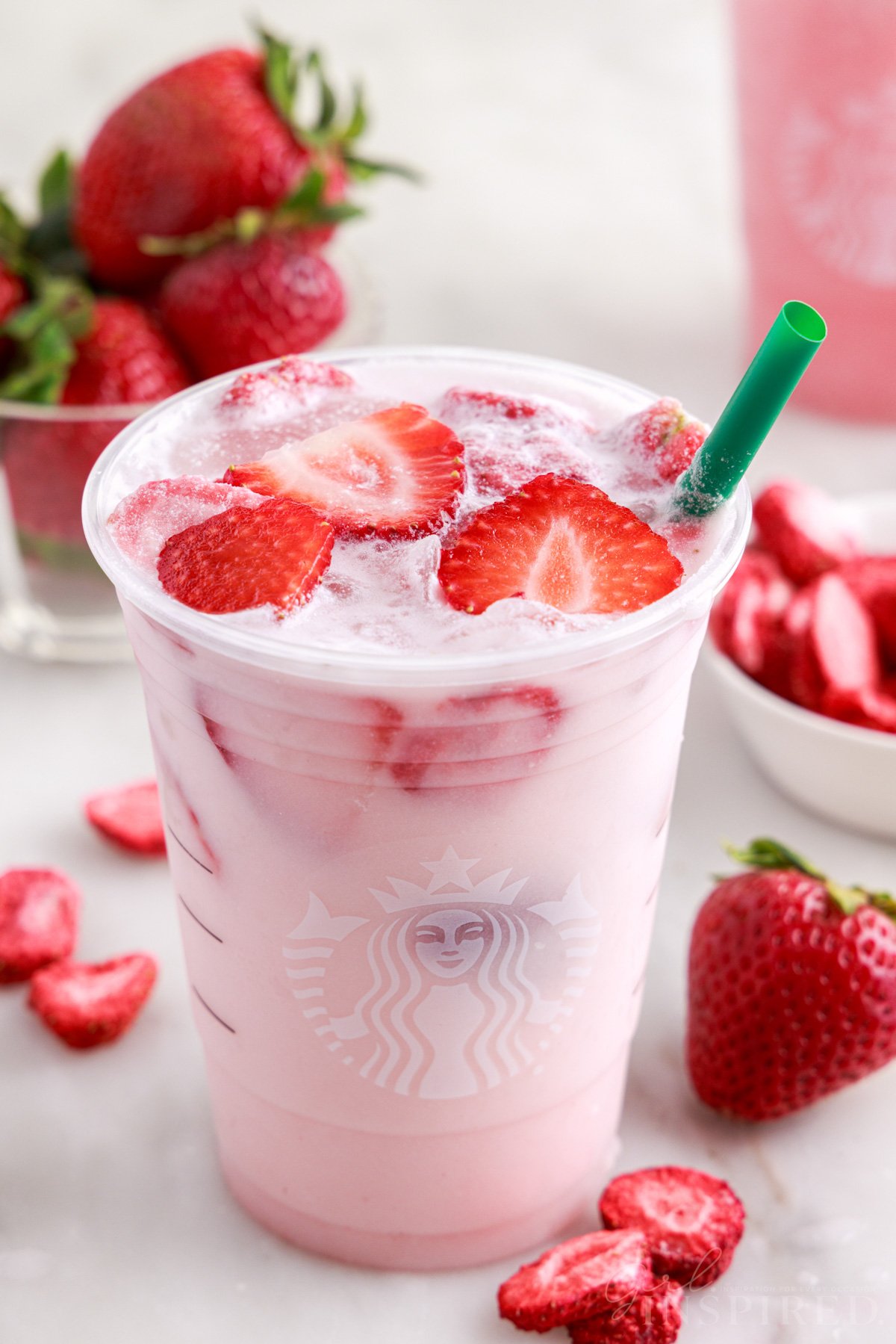 Pink drink recipe filling plastic Starbucks cup with freeze dried strawberries and fresh strawberry slices floating in drink.
