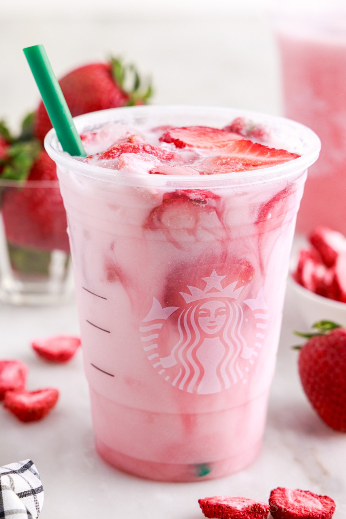 Pink drink recipe filling plastic Starbucks cup with freeze dried strawberries floating in drink.