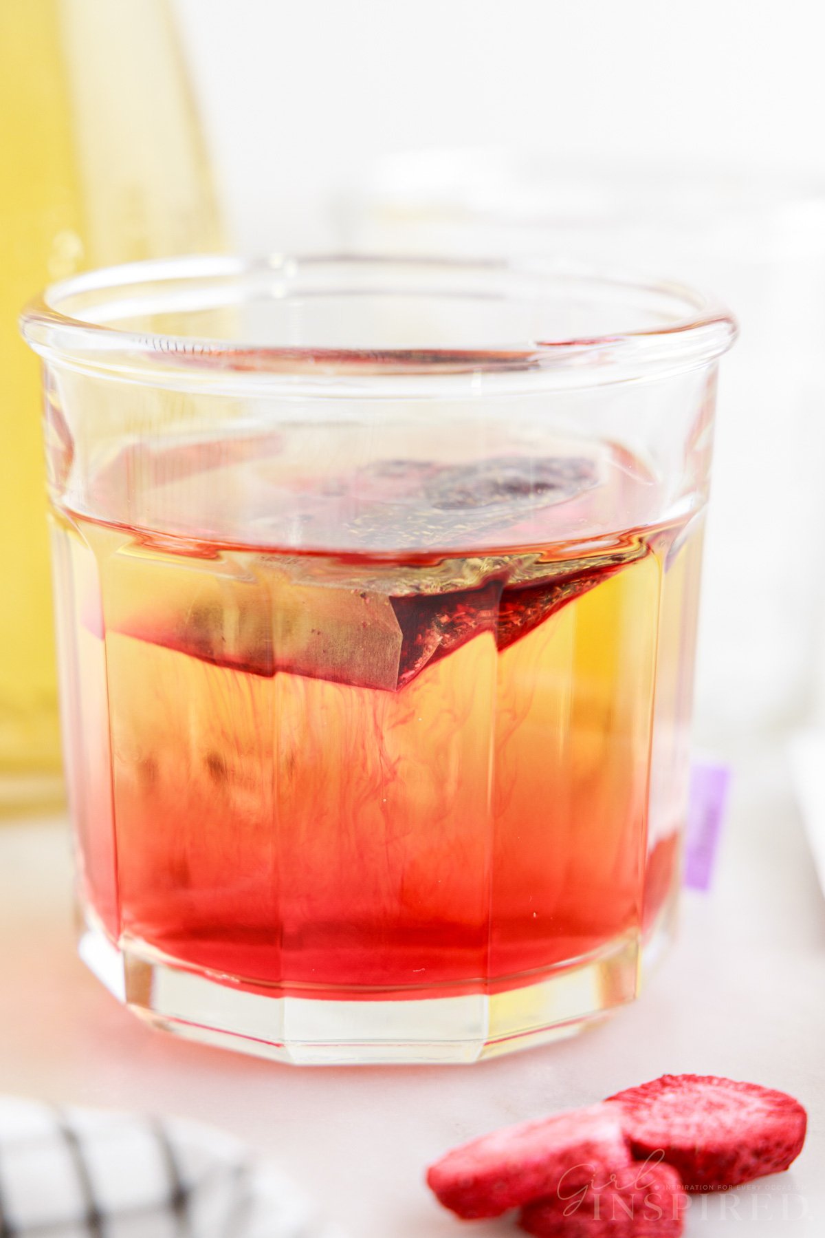 Bright pink tea seeping into the yellow-hued white grape juice in a cup.