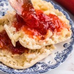 Two halves of a scone topped with strawberry rhubarb jam on a fine china plate, on a white surface