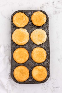 Baked white cupcakes in muffin tray, white linen, on a white marble countertop