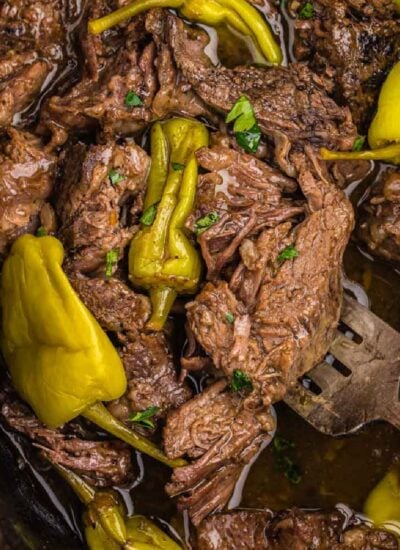 Crock pot Mississippi pot roast in bowl of slow cooker with fork lifting shredded meat and whole pepperoncinis.