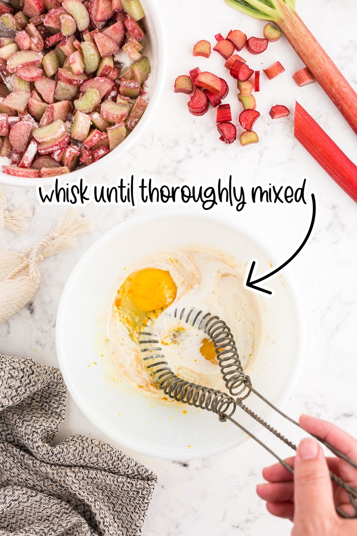 Beating egg and milk in a mixing bowl, flour/rhubarb mixture in a nearby bowl. Text overlay reads "whisk until thoroughly mixed."