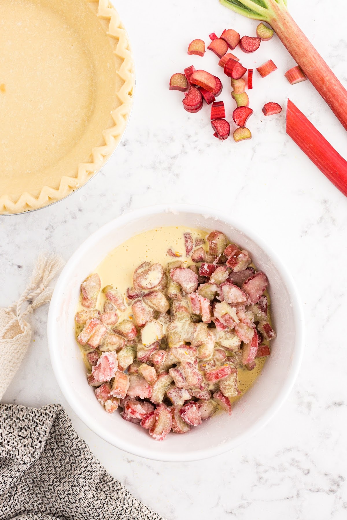 Rhubarb pieces and custard mixture together in a bowl with unbaked pie crust nearby.