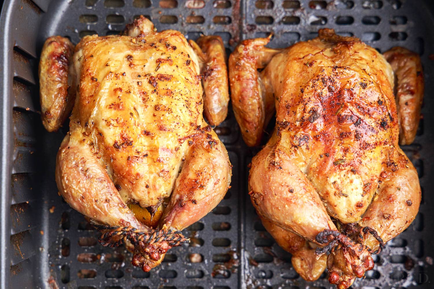 close up of two finished air fryer cornish hens in an air fryer basket