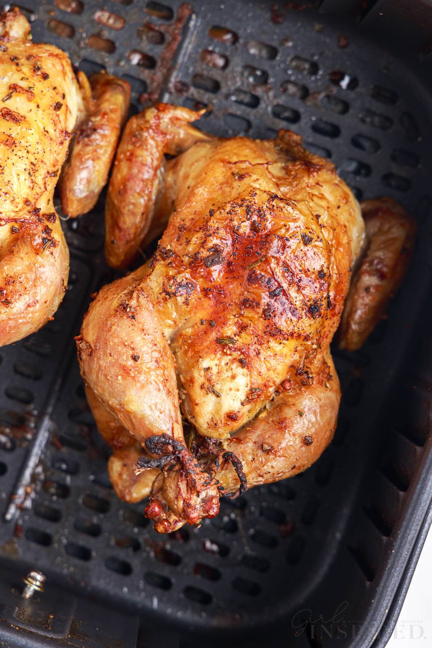 overview of a finished air fryer cornish hen in an air fryer basket next to another cornish hen