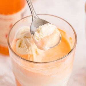 Spoon scooping vanilla ice cream and some orange soda fizz from a glass of boozy creamsicle float.
