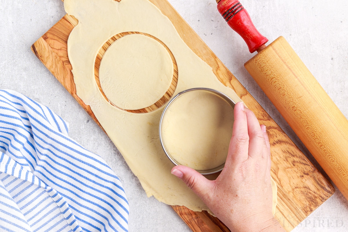 cutting out dough circles with a cookie cutter next to a rolling pin