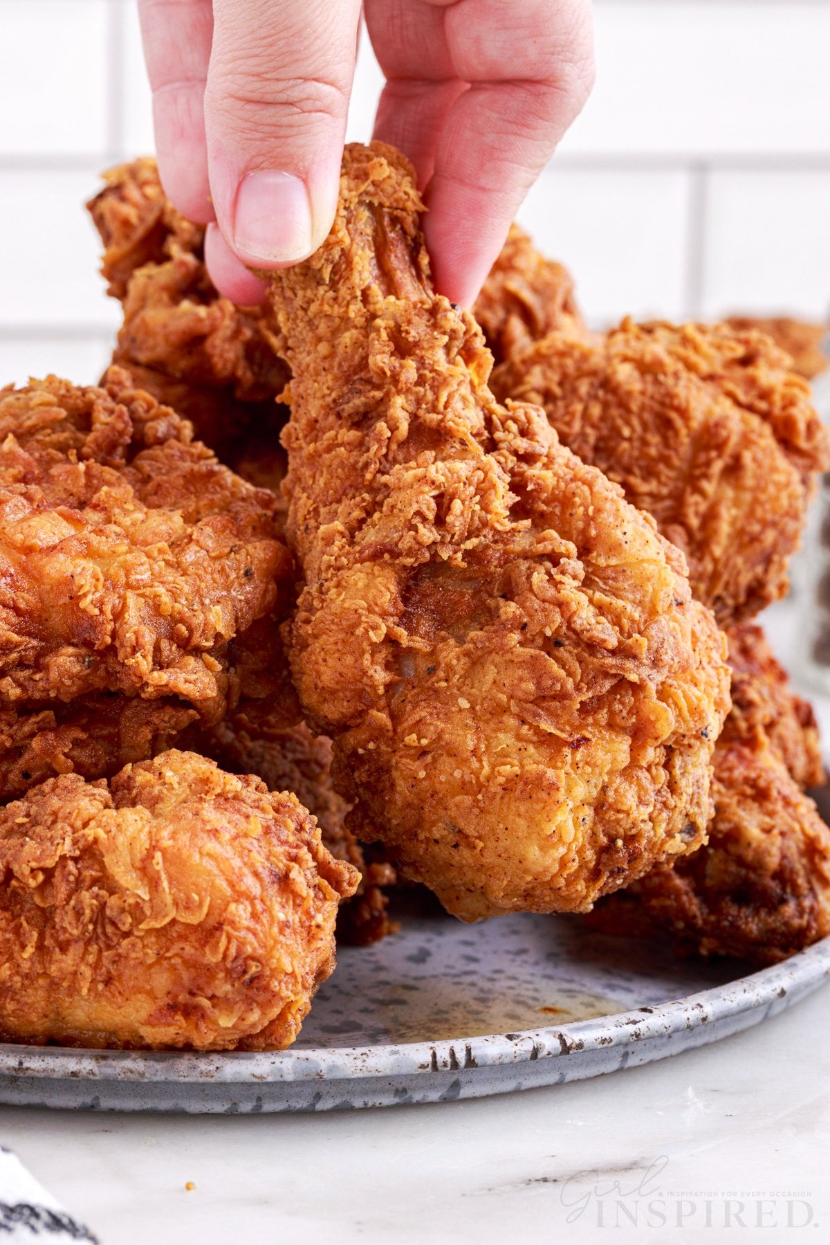 lifting a southern fried chicken drumstick above the dish of fried chicken
