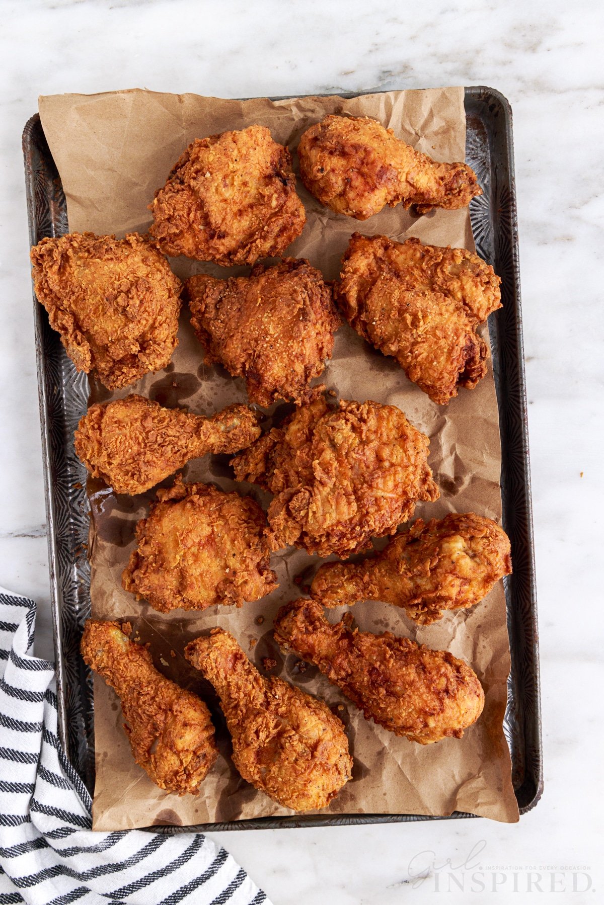 Fried chicken on a metal baking tray on a white marble countertop, navy striped linen.