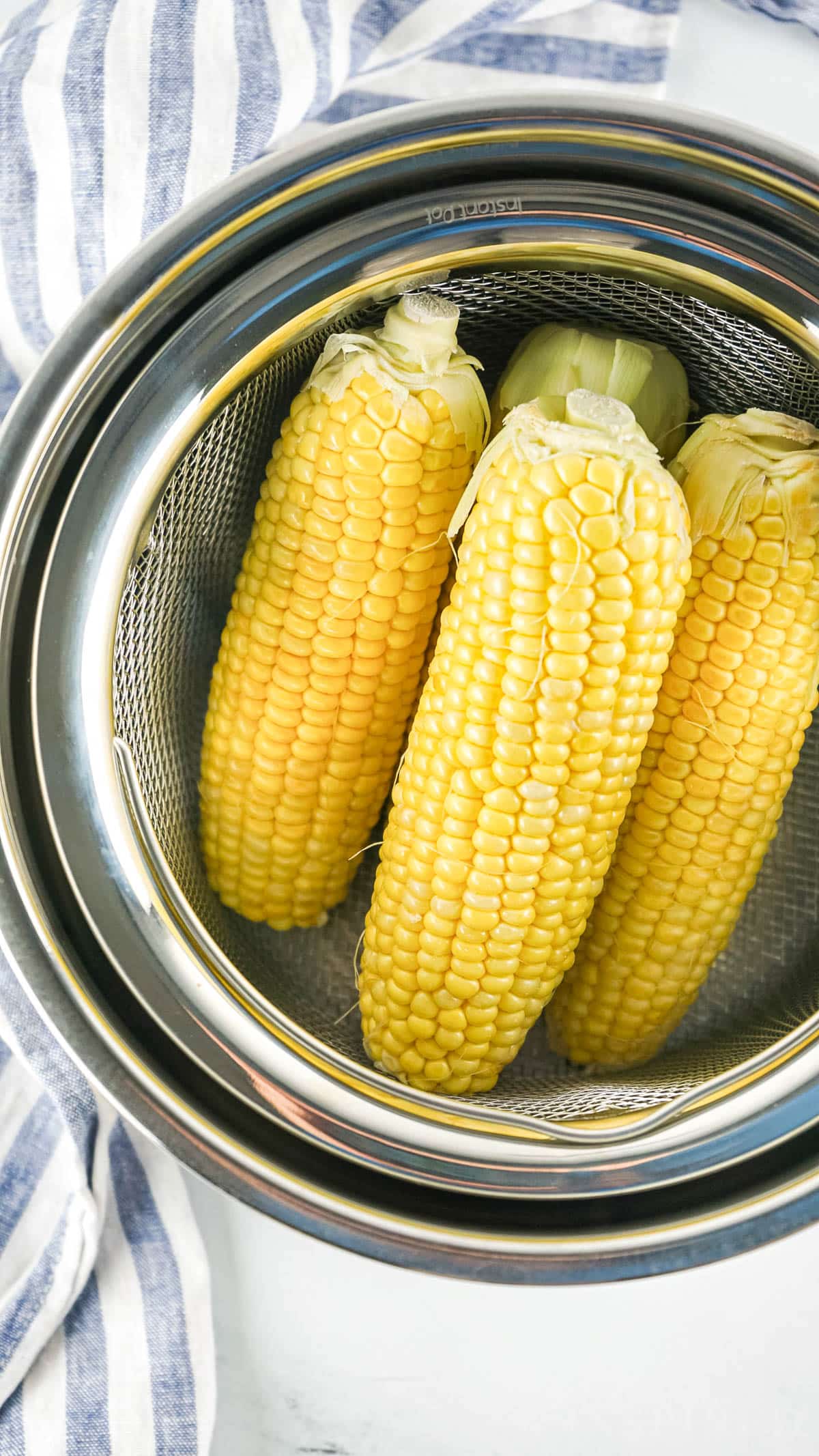 Ears of corn stacked inside a steamer basket in the instant pot.