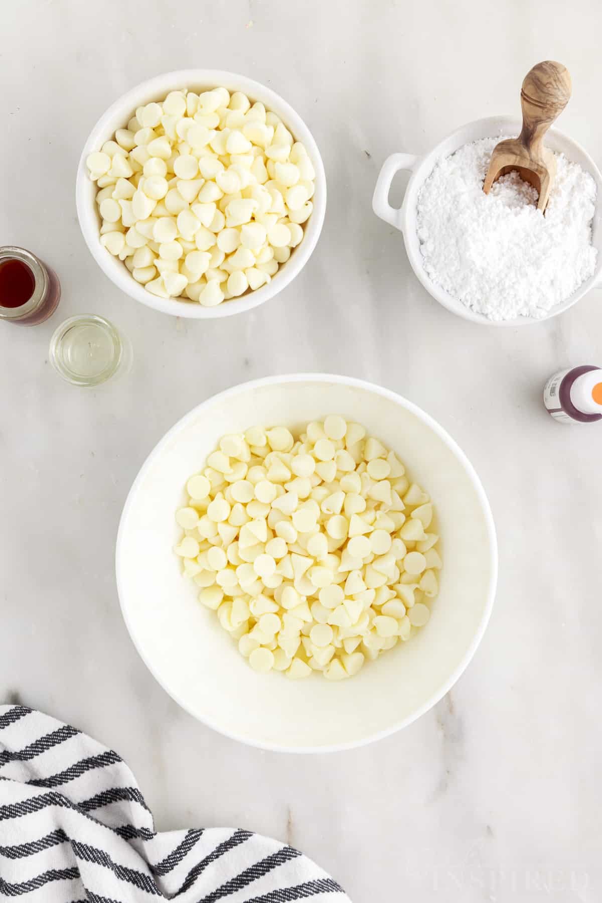 Bowl filled with white chocolate chips next to bowl of more chips and powdered sugar.