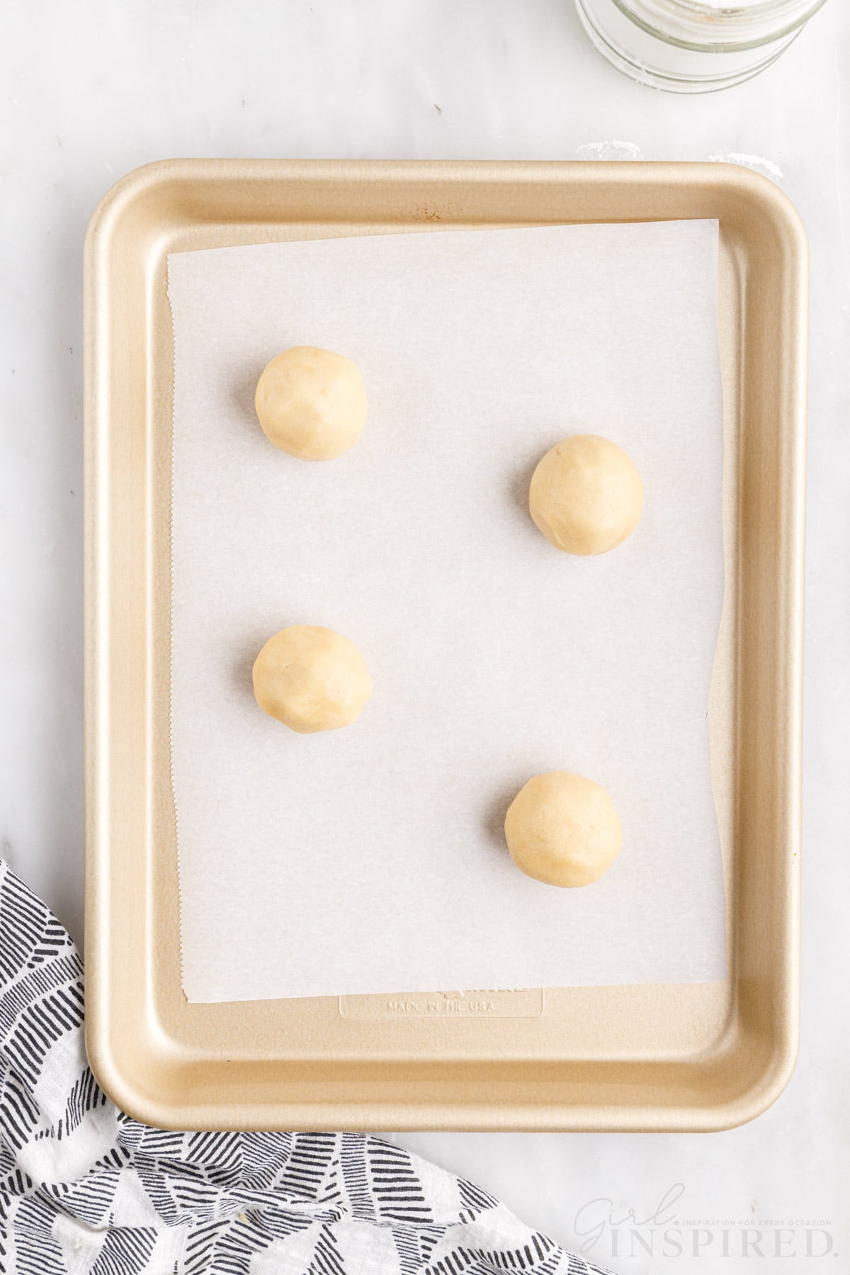 four sugar cookie dough balls on a parchment lined baking sheet