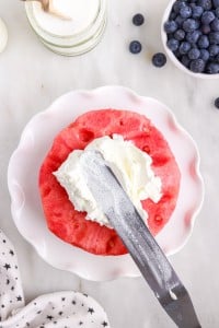 frosting the first layer of watermelon with whipped topping