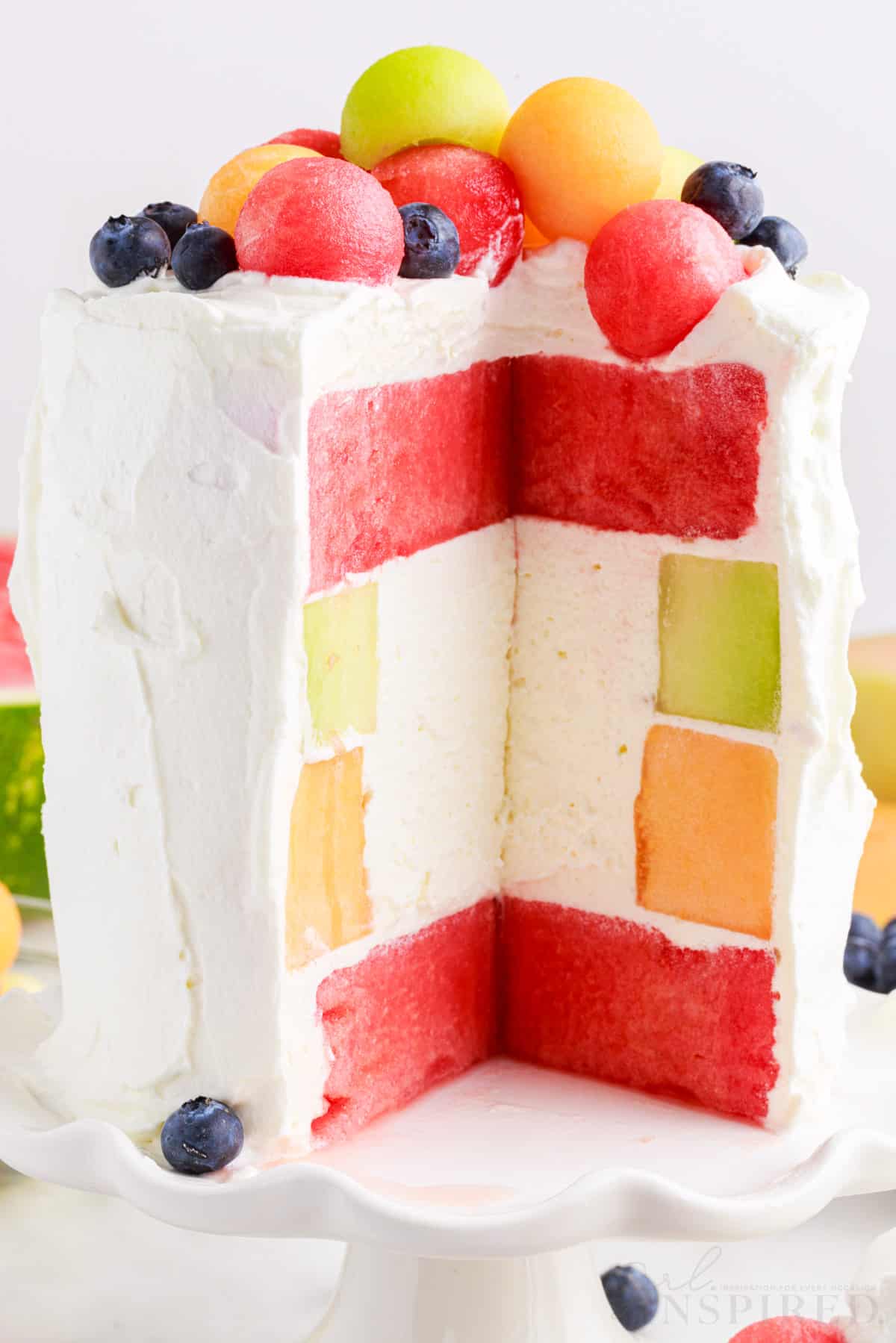 Close up of whipped cream watermelon cake topped with balled fruit.