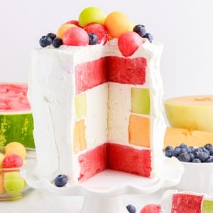 watermelon cake on a stand next to fresh fruit