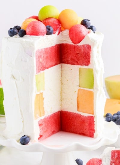 watermelon cake on a stand next to fresh fruit