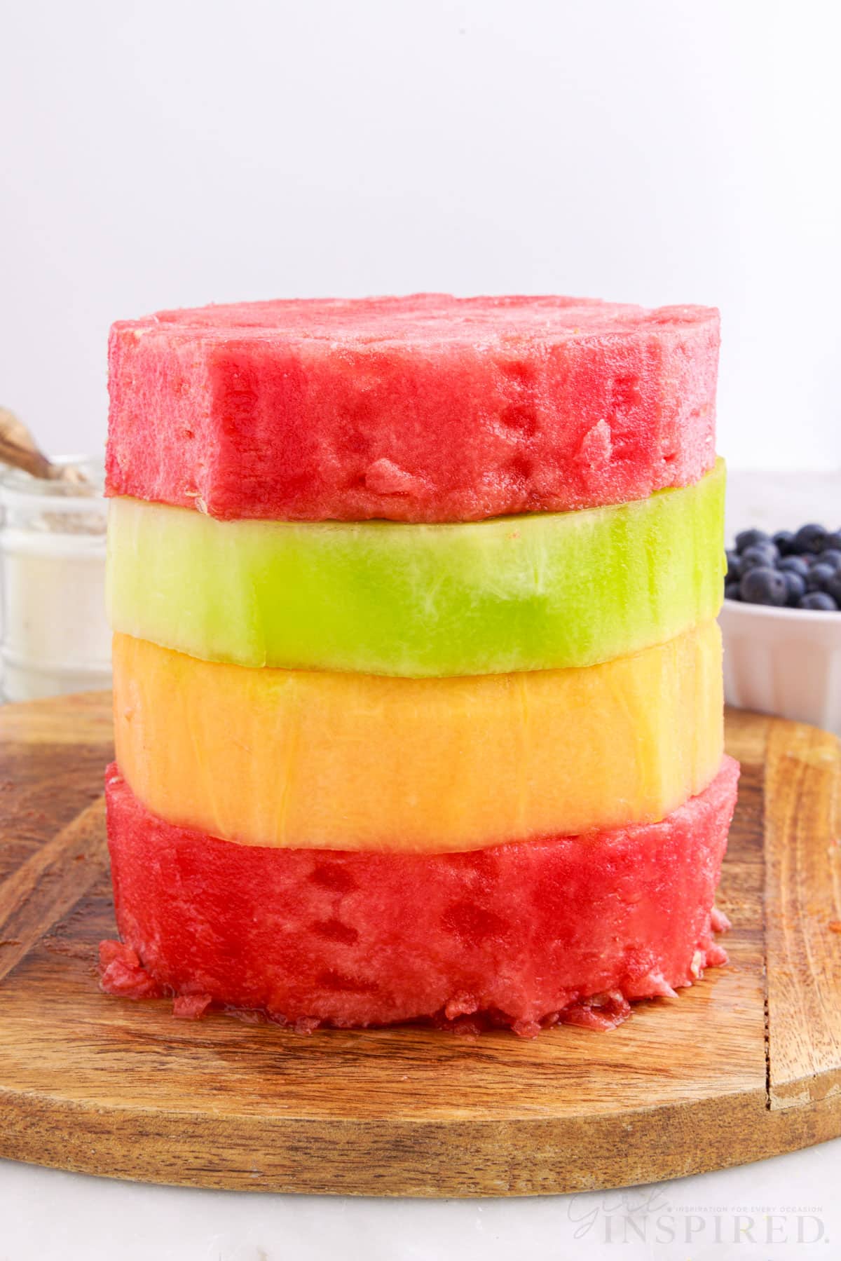 watermelon stacked on top of honeydew and cantaloupe sitting on a cutting board
