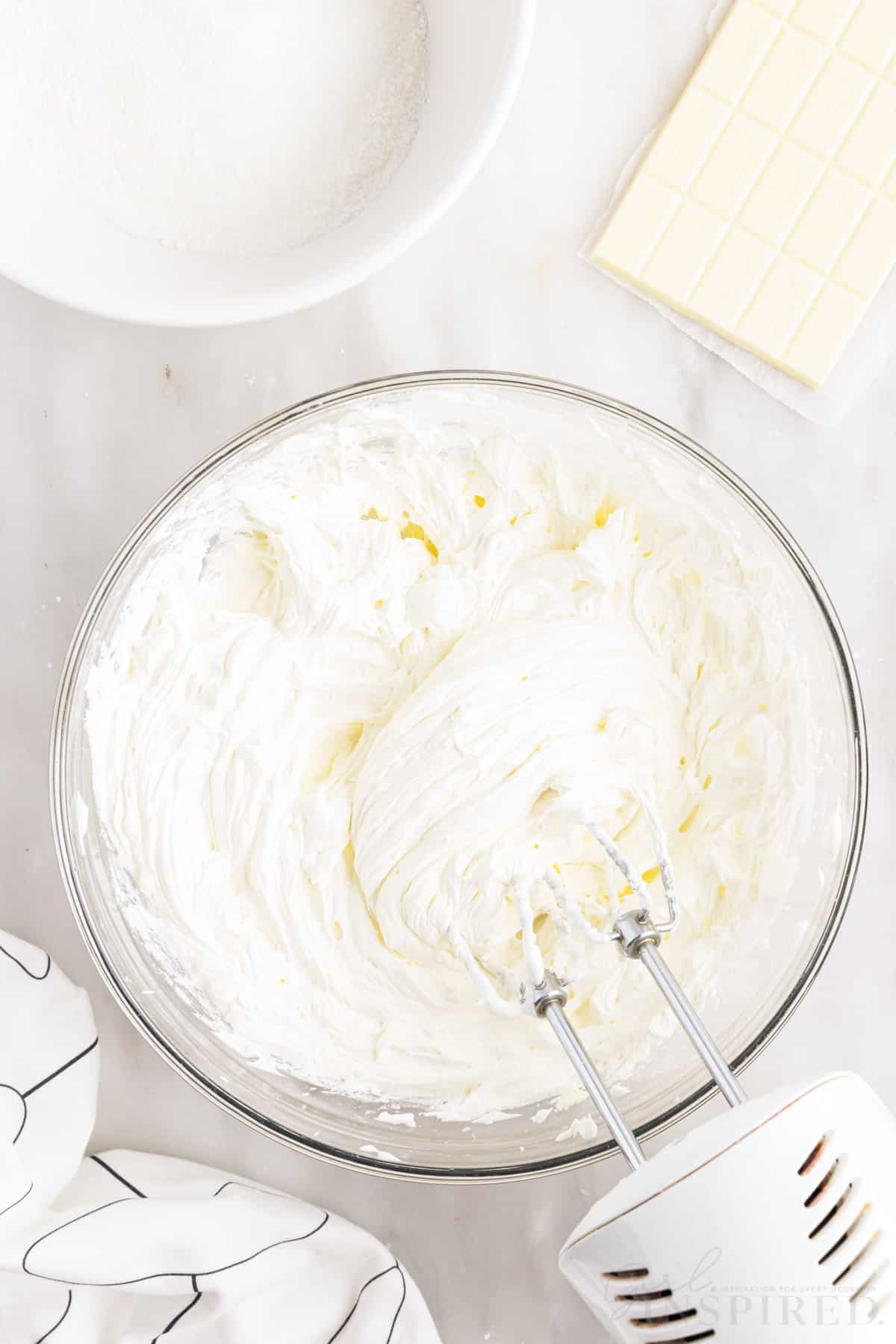 whipped cream layer after being mixed with the electric mixer resting on the side of the bowl