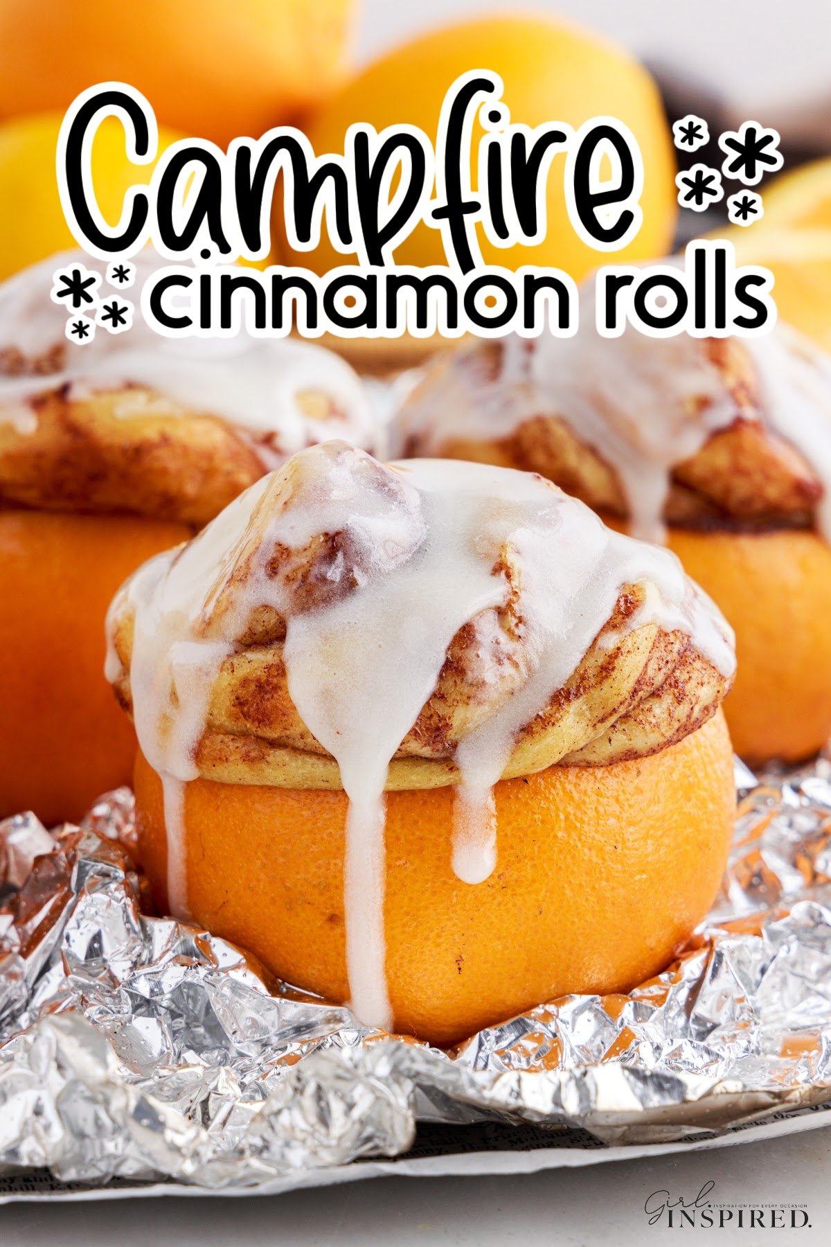 Orange wrapped in aluminum foil stuffed with a baked cinnamon roll dripping with frosting and text title "campfire cinnamon rolls."