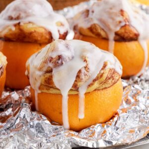 campfire cinnamon rolls drizzled with icing stuffed into an orange