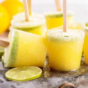 Margarita Popsicles standing on metal ice pack next to fresh lime wheels.
