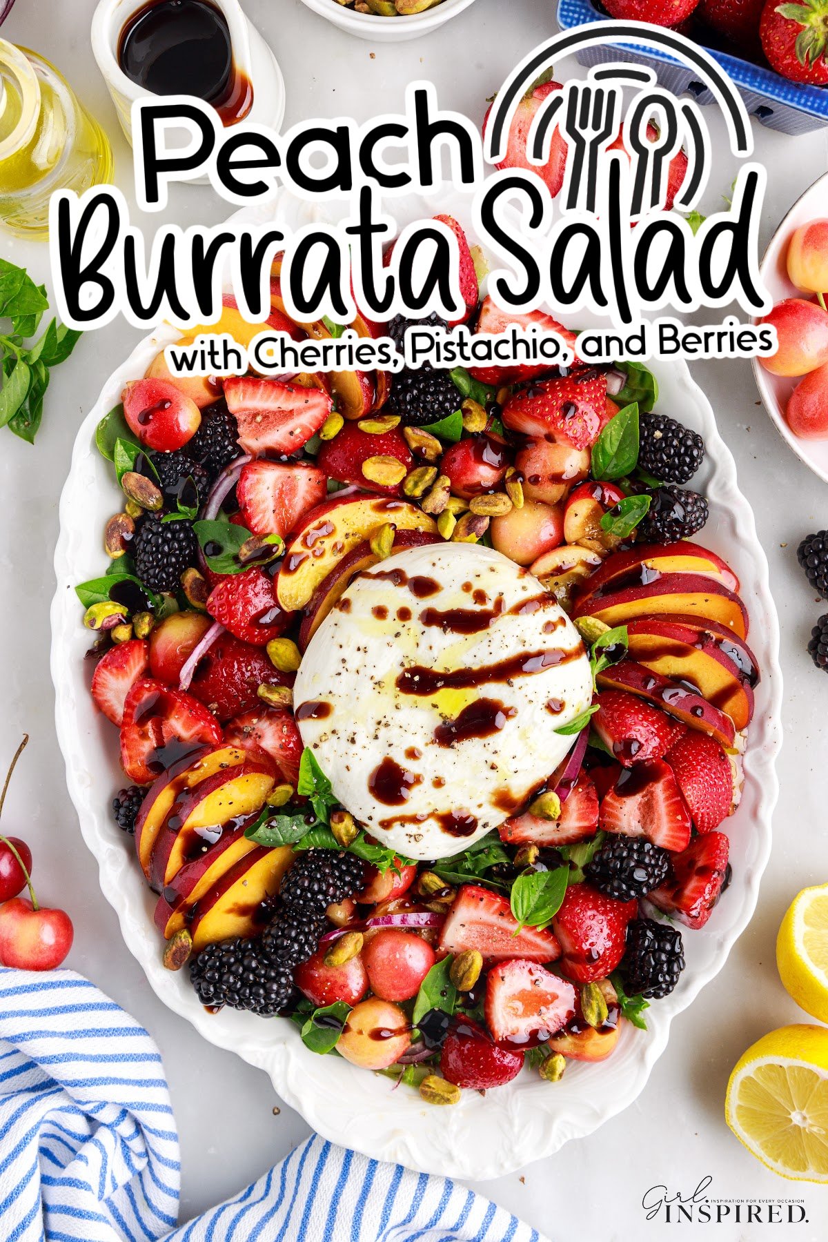 Peach burrata salad featuring sliced peaches, strawberries, blackberries, greens, cherries, pistachios, and a ball of burrata cheese in the center of a large serving platter.